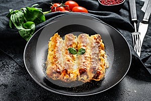 Italian homemade pasta cannelloni with beef and tomato sauce. Black background. top view
