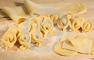 Italian homemade tortellini and raw handmade dough,placed on wooden table and sprinkled with flour.