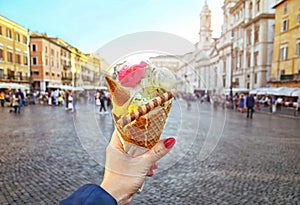 Italian ice - cream cone held in hand on the background of Piazza Navona in Rome , Italy