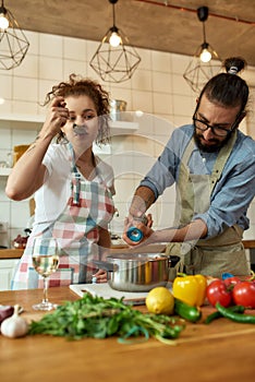 Italian man adding pepper, spice to the soup while woman tasting it. Couple preparing a meal together in the kitchen