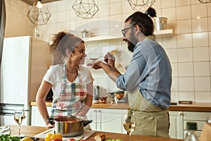 Italian man, chef cook feeding his girlfriend, letting her taste the soup. Cheerful couple preparing a meal together in