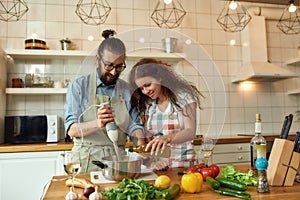 Italian man, chef cook using hand blender while preparing a meal. Young woman, girlfriend in apron pouring olive oil in