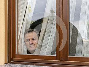 Italian man forced to remain in quarantine because of the coronavirus covid-19 peeps through the window