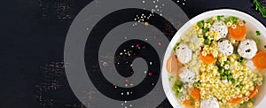 Italian meatball soup and Stelline gluten free pasta in bowl on black table.