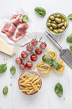 Italian or mediterranean food cuisine and ingredients on white concrete table. Tagliatelle pene pasta olives olive oil tomatoes