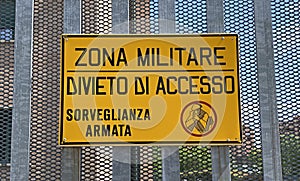 Italian military area with yellow sign: `Military zone, no entry, armed surveillance`. photo