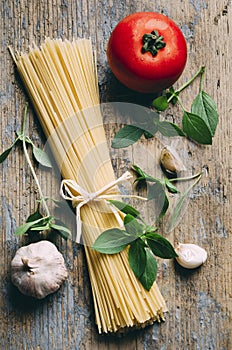 Italian pasta food ingredients on rustic wooden table from above. Top view of spaghetti, garlic, tomato and basil for bolognese