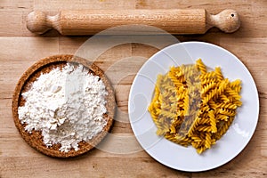 Italian pasta, fusilli. Rolling pin, flour. Wooden surface.