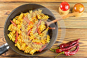 Italian pasta fusilli with tomato sauce and sausage in pan, wooden spoon, red pepper on table, top view, space for text