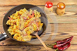 Italian pasta fusilli with tomato sauce and sausage in pan, wooden spoon, red pepper on table, top view, space for text