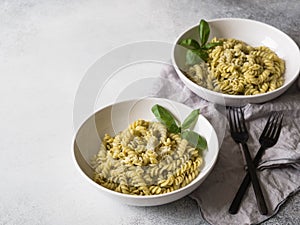 Italian pasta with pesto sauce, fresh basil and Parmesan in a white bowls on grey background. Cope space