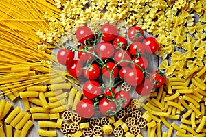 Italian pasta rigatoni, penne, maccheroni, spaghetti, farfalle and tomato on wooden background