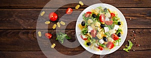 Italian pasta salad with fresh tomato, cheese, lettuce and olives on wooden background. Mediterranean cuisine. Banner