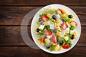 Italian pasta salad with fresh tomato, cheese, lettuce and olives on wooden background. Mediterranean cuisine. Cooking lunch. Hea