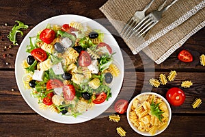 Italian pasta salad with fresh tomato, cheese, lettuce and olives on wooden background. Mediterranean cuisine. Cooking lunch. Hea