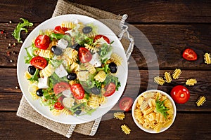 Italian pasta salad with fresh tomato, cheese, lettuce and olives on wooden background. Mediterranean cuisine. Cooking lunch. Hea