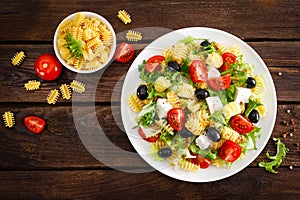 Italian pasta salad with fresh tomato, cheese, lettuce and olives on wooden background. Mediterranean cuisine. Cooking lunch. Hea