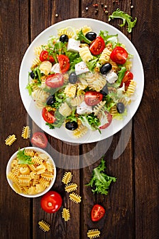 Italian pasta salad with fresh tomato, cheese, lettuce and olives on wooden background. Mediterranean cuisine. Cooking lunch. Hea