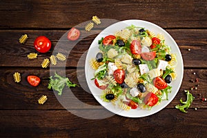 Italian pasta salad with fresh tomato, cheese, lettuce and olives on wooden background. Mediterranean cuisine. Cooking lunch. Hea