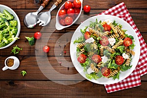 Italian pasta salad with wholegrain fusilli, fresh tomato, cheese, lettuce and broccoli on wooden rustic background