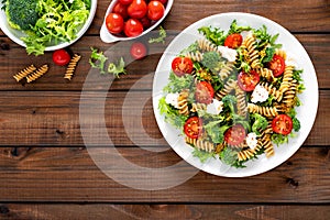 Italian pasta salad with wholegrain fusilli, fresh tomato, cheese, lettuce and broccoli on wooden rustic background