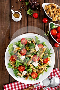 Italian pasta salad with wholegrain fusilli, fresh tomato, cheese, lettuce and broccoli on wooden rustic background