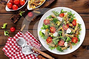 Italian pasta salad with wholegrain fusilli, fresh tomato, cheese, lettuce and broccoli on wooden rustic background