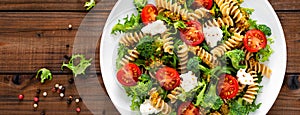 Italian pasta salad with wholegrain fusilli, fresh tomato, cheese, lettuce and broccoli on wooden rustic background