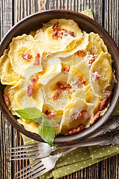 Italian pasta in the shape of a sunflower Girasoli stuffed with cheese, bacon and basil close-up in a plate on the table. Vertical photo