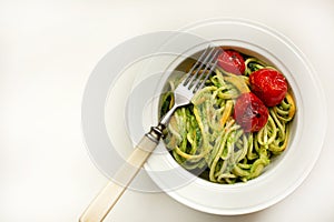 Italian Pasta with zucchini noodles with Avocado Sauce pesto and roasted tomato in white plate and fork. Top view white