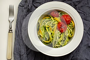 Italian Pasta with zucchini noodles with Avocado Sauce pesto and roasted tomato in white plate. Top view gray textile