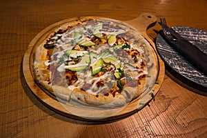 Italian pizza with avocado and grilled chicken served on a wooden board