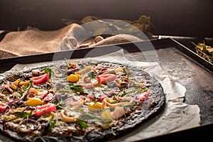 Italian pizza with black dough and seafood on a baking tray from the oven