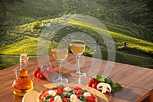 Italian pizza with glasses of white wine against Tuscan vineyards near the Florence in Italy