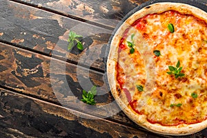 Italian pizza Margherita with cheese, tomato sauce and basil on dark wooden table top view with copy space for yor text