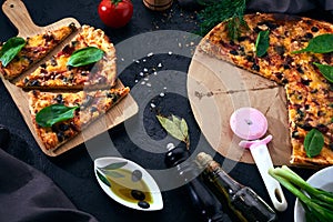 Italian pizza and pizza cooking ingredients on dark background. Tomatoes, olives oil, herbs, salt and spices