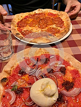Italian pizzeria, pizzas in two flavors on the table, pizza with bufala mozzarella, pizza with schiacciata salami, classic Italian