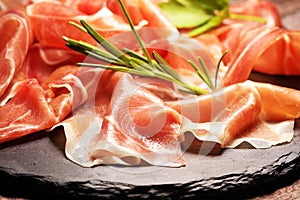 Italian prosciutto crudo or jamon with rosemary. Raw ham on wooden board