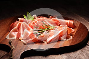 Italian prosciutto crudo or jamon with rosemary. Raw ham on wooden board photo