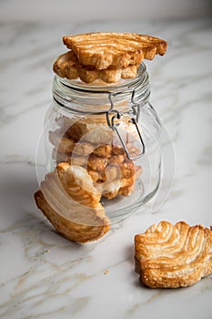 Italian puff pastry fan wavers cookies biscuits with preserving glass jar on marble table background