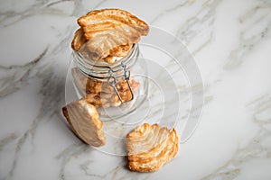 Italian puff pastry fan wavers cookies biscuits with preserving glass jar on marble table background