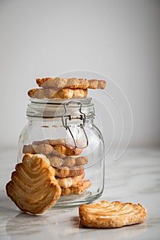 Italian puff pastry fan wavers cookies biscuits with preserving glass jar on marble table background