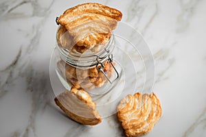 Italian puff pastry fan wavers cookies biscuits with preserving glass jar on marble table background