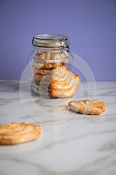 Italian puff pastry fan wavers cookies biscuits with preserving glass jar on marble table and lilac background