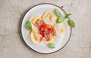 Italian ravioli with meat tomato sauce and basil leaves with on a white dishes on concrete background