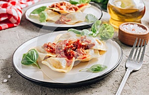 Italian ravioli with meat tomato sauce and basil leaves with on a white dishes on concrete background.