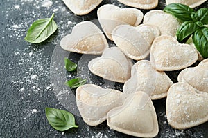 Italian ravioli pasta in heart shape. Tasty raw ravioli with flour and basil on dark background. Food cooking ingredients