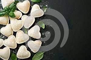 Italian ravioli pasta in heart shape. Tasty raw ravioli with flour and basil on dark background. Food cooking ingredients backg