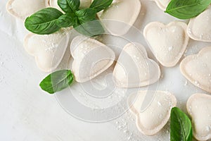 Italian ravioli pasta in heart shape. Tasty raw ravioli with flour and basil on white background. Food cooking ingredients backgr