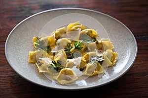 Italian ravioli on white ceramic plate, looking  tasty and appetizing with cheese and parsley selective focus on rustic table
